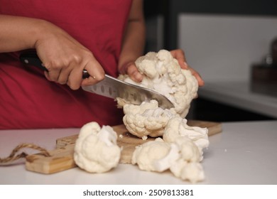 Close-up of hands using a large knife to cut a head of cauliflower on a wooden cutting board, showcasing the preparation of fresh ingredients. This image reflects the importance of home cooking with - Powered by Shutterstock