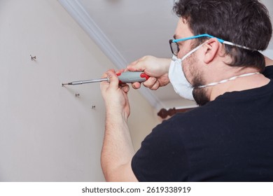 Primer plano de las manos utilizando un destornillador manual para instalar un tornillo en un anclaje de pared. Persona que usa gafas de seguridad y máscara durante la reparación del hogar o el proyecto de bricolaje.