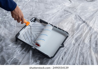 Close-up of hands using paint roller and white paint on the paint tray. Home improvement and house painting concept.