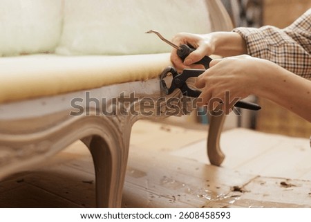 Close-up of hands using pliers and a screwdriver to remove old staples from vintage furniture during reupholstery.