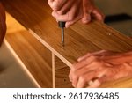 Close-up of hands using a screwdriver to assemble wooden furniture. Represents DIY, home improvement, and craftsmanship.

