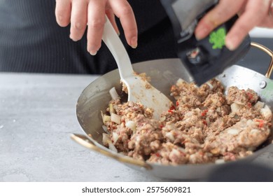 Close-up of hands using white spatula mixing ground meat with onions and spices in a wok