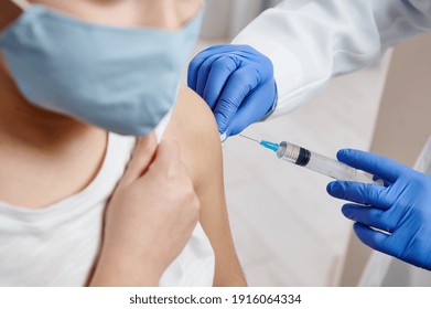 Closeup of hands wearing medical protective gloves holding syringe and making vaccine injection on a child arm