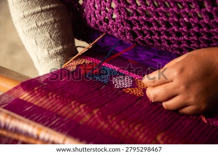 Close-up of hands weaving intricate patterns on a vibrant purple textile. Handmade textiles in Chiapas, Mexico.