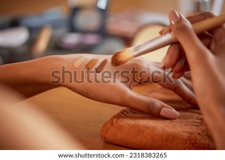 Closeup of hands of woman applying different shades of liquid foundation on hand before makeup. Latin girl testing skin tone complexion on hand with brush at beauty salon. 