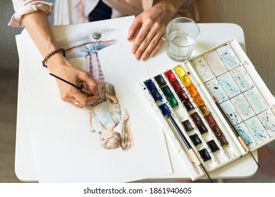 Close-up, hands of a woman artist, view from the top, a girl on a skateboard draws a picture, a color palette on the table, a glass cup with water background - Powered by Shutterstock