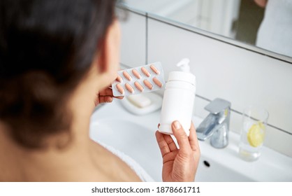 Closeup of hands of woman holding a bottle with medical tablets on one hand and blister pack with orange pills on the other. - Shutterstock ID 1878661711