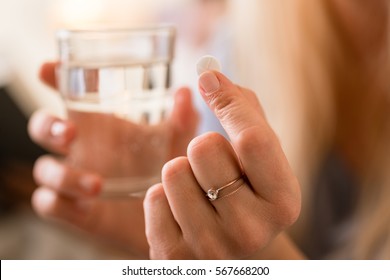 Close-up of the hands of a woman holding a pill and a glass of water