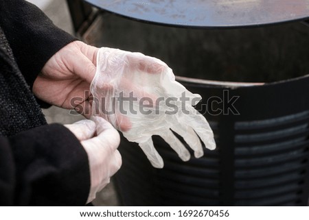Closeup of hands of woman putting used latex gloves in the garbage in the street 