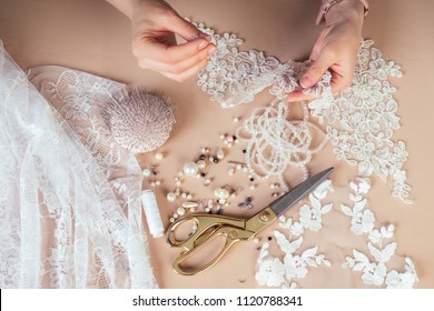 close-up hands of woman seamstress tailor ( dressmaker) designer wedding dress sews beads to lace on a blue background in the studio