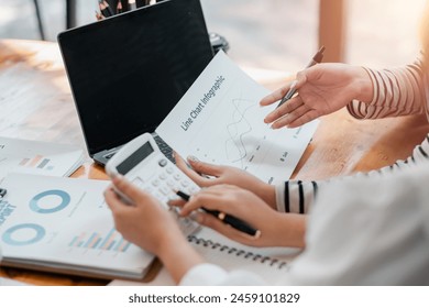 Close-up of hands working with a calculator and analyzing statistical data on line charts, with a laptop in the background. - Powered by Shutterstock