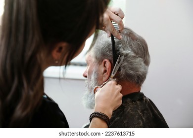 Closeup hands working with hair scissors. Professional hairstyler woman cutting hair of mature man. He is getting haircut at barbershop or beauty salon. - Shutterstock ID 2237613715