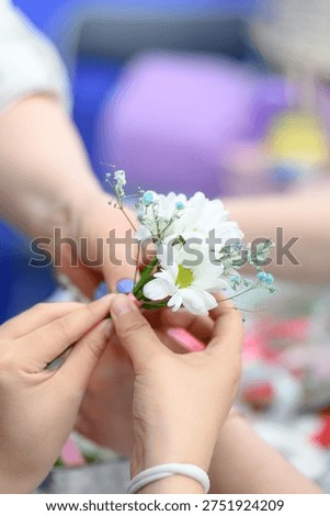 Close-up of hands working together to create a floral arrangement featuring white flowers and delicate greenery, with a colorful background