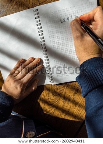 Close-up of hands writing IDEA in a notebook on a wooden desk in sunlight. High quality photo