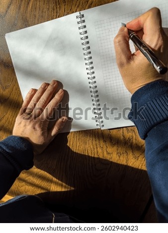 Close-up of hands writing IDEA in a notebook on a wooden desk in sunlight. High quality photo