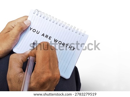Close-up of hands writing “You Are Worthy” in a notebook, symbolizing self worth, motivation, encouragement, mental wellness, and positive affirmation.