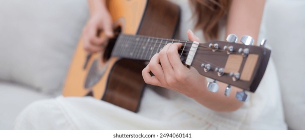 Closeup hands of young asian woman sitting on sofa playing guitar in living room at home, skill and practice, guitarist and hobby with enjoyment and relax, entertainment and lifestyle. - Powered by Shutterstock