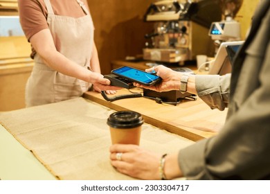 Close-up of hands of young consumer with smartphone and bakery clerk with terminal during process of contactless payment over counter - Powered by Shutterstock