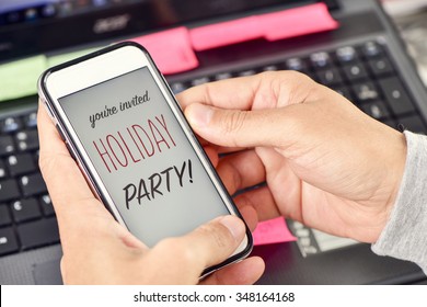 Closeup Of The Hands Of A Young Man At His Office Holding A Smartphone With The Text You Are Invited Holiday Party In Its Screen