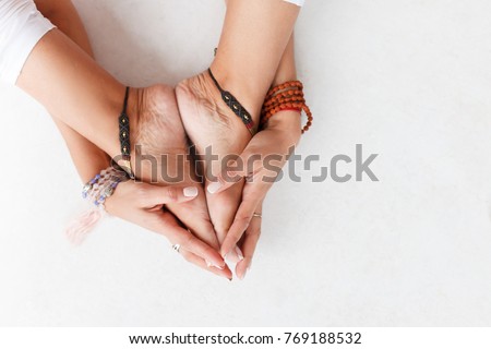 Close-up - hands of young unidentified woman hugging folded feetÂ with bracelets on white isolated background