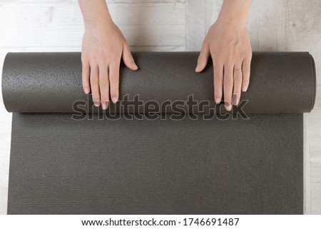 Close-up, hands of a young woman folding a yoga or fitness Mat after a workout at home in the living room. Healthy life, keep yourself in the shape of a concept. Horizontal shot