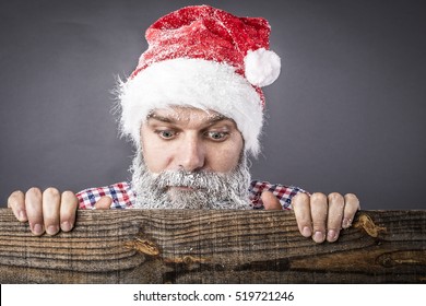 Closeup of a  handsome man with frozen beard and mustache wearing red santa claus and looking down over the fence over gray background