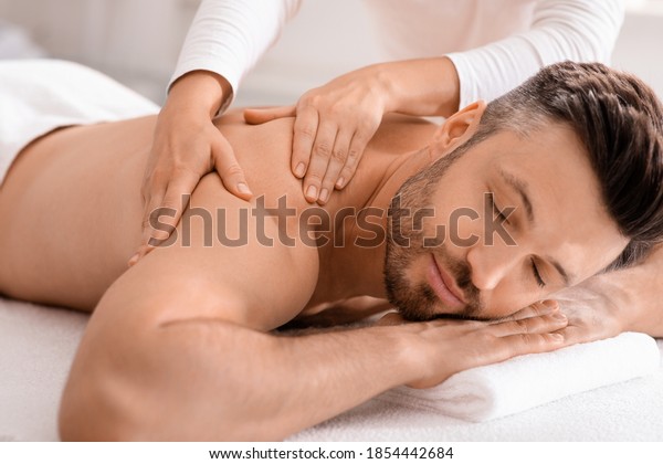 Closeup of handsome man having full body massage at\
male spa. Unrecognizable female therapist rubbing middle aged man\
shoulders, making relaxing massage. Spa, massage, cosmetology for\
men