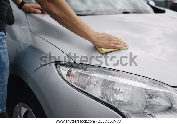Close-up of\
handsome man wipes a car with a rag in a showroom at a self-service\
car wash. Gray car. Back\
view
