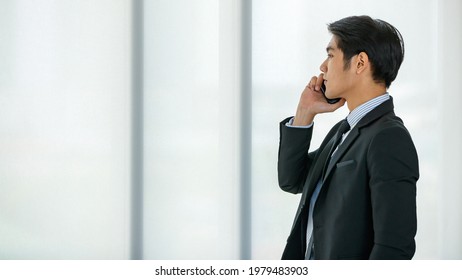 Closeup handsome young Asian businessman wearing formal suit, showing happy expression, smiling with confidence while talking mobile phone, presenting about technology and convenient communication - Shutterstock ID 1979483903