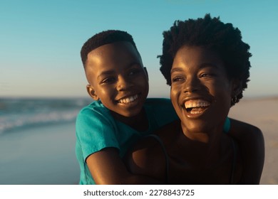 Closeup of happy african american mother piggybacking son at beach against blue sky at sunset. Copy space, unaltered, family, together, childhood, nature, vacation, enjoyment and summer concept. - Powered by Shutterstock