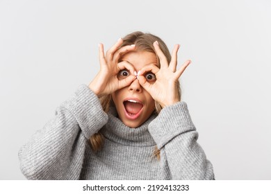 Close-up Of Happy Attractive Girl Having Fun, Looking Through Finger Glasses And Look Amazed, Standing Over White Background