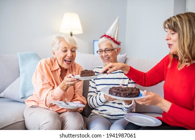 Close-up Of Happy, Excited Pensioners During A Birthday Party. Active Seniors Concept. Senior Woman Blows Out Birthday Cake Candles At Family Party. Seniors Celebrating A Birthday In A Retirement Home