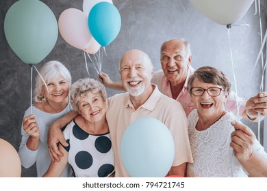 Close-up of happy, excited pensioners during a birthday party, holding colorful balloons. Active seniors concept.