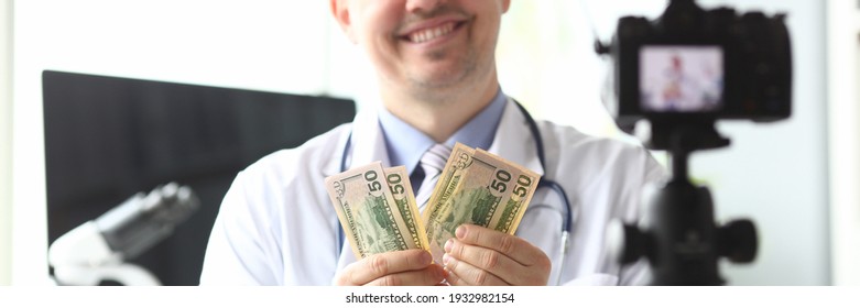 Close-up of happy person looking at camera with happiness. Successful smiling blogger counting earned money in front of videocamera. Blogging and vlogging concept