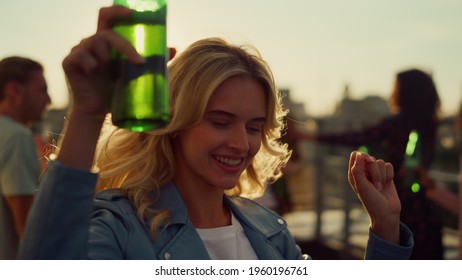 Closeup happy woman enjoying party with beer bottle at sunset rooftop. Laughing girl dancing with raised hands at disco outdoors. Beautiful female dancer having fun with friends outside.  - Powered by Shutterstock