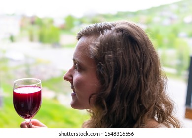 Closeup Of Happy Woman Tasting Red Wine By View Of Crested Butte Snow Mountains From Apartment Balcony Window