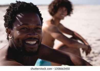 Close-up of happy young African American man smiling to the camera on the beach with his friend on the background - Powered by Shutterstock