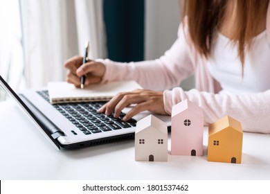 Closeup Of A Happy Young Asian Woman Searching Home Information Online With A Laptop And Writing On Notebook On A Table At Home. Mortgage And Real Estate Property Investment Concept.