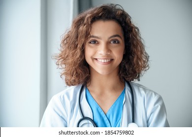 Close-up Of Happy Young Female Doctor Wear Blue Uniform, White Medical Coat, Stethoscope And Looking At Camera In Hospital Office. Portrait Of Beautiful Hispanic Female Doctor, Therapist, Nurse.