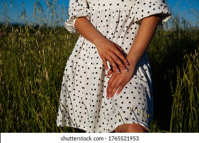 Closeup of happy young woman wearing white summer dress  on sunny day outdoors.Woman's hand in sunset light.Girl touching her dress at sunset in meadow grass.The woman's hands on a dress.