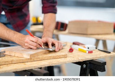 Close-up of a hardworking professional carpenter holding a angular ruler and pencil while measuring a board in a carpentry workshop. A bearded DIY enthusiast measures wood. There are a locksmith table - Shutterstock ID 1905078391