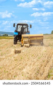 Close-up of hay baling with a tractor using a baler on a cloudy summer day, a large bale comes out of the baler. 