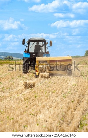 Close-up of hay baling with a tractor using a baler on a cloudy summer day, a large bale comes out of the baler. 