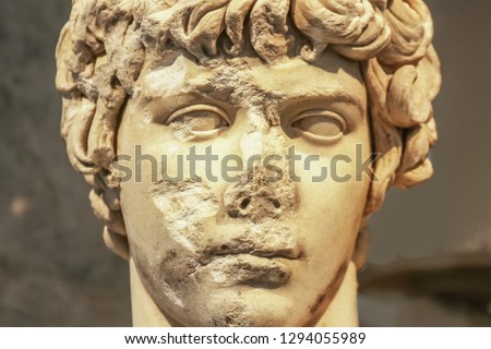 Close-up of head of ancient marble statue of attractive Greek youth with parts of face chipped off and destroyed