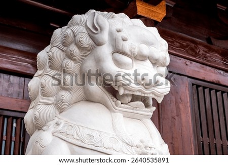 A close-up of the head of a white marble lion statue in a Chinese classical garden