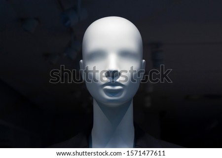 A close-up of a mannequin’s head in a window of a mall on the dark background with switched off electric lamps on the ceiling. Copy space.