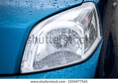 Close-up of the headlight of a blue car under the rain