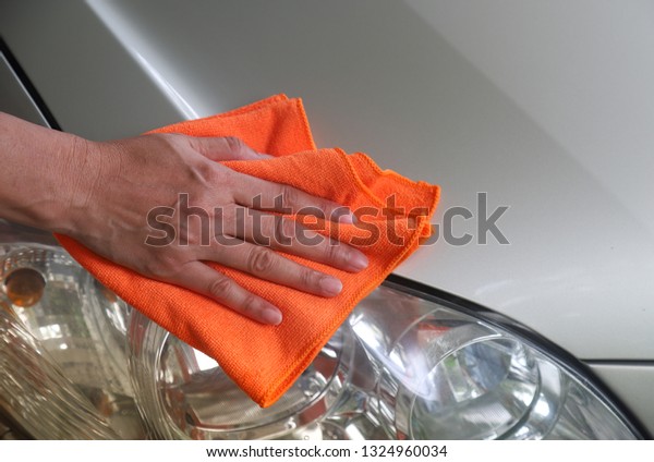Closeup of headlight of golden car\
cleaning  by woman owner\'s hand with orange  microfiber cloth in\
sunny day. Lovely family activity in simply way of\
life.