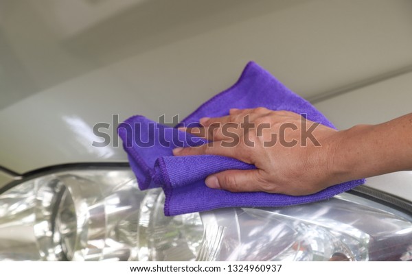 Closeup of headlight of golden car\
cleaning  by woman owner\'s hand with blue microfiber cloth in sunny\
day. Lovely family activity in simply way of\
life.