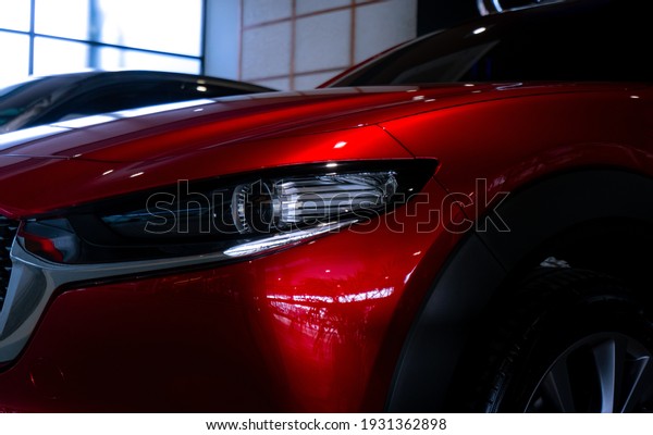 Closeup headlight of shiny red luxury SUV\
car in showroom. Elegant electric car with sport design. Car parked\
in showroom. Car dealership. Electric vehicle development concept.\
Future transportation.